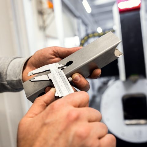 Close up of mans hands inspecting laser cut of metal square tube with vernier caliper.
